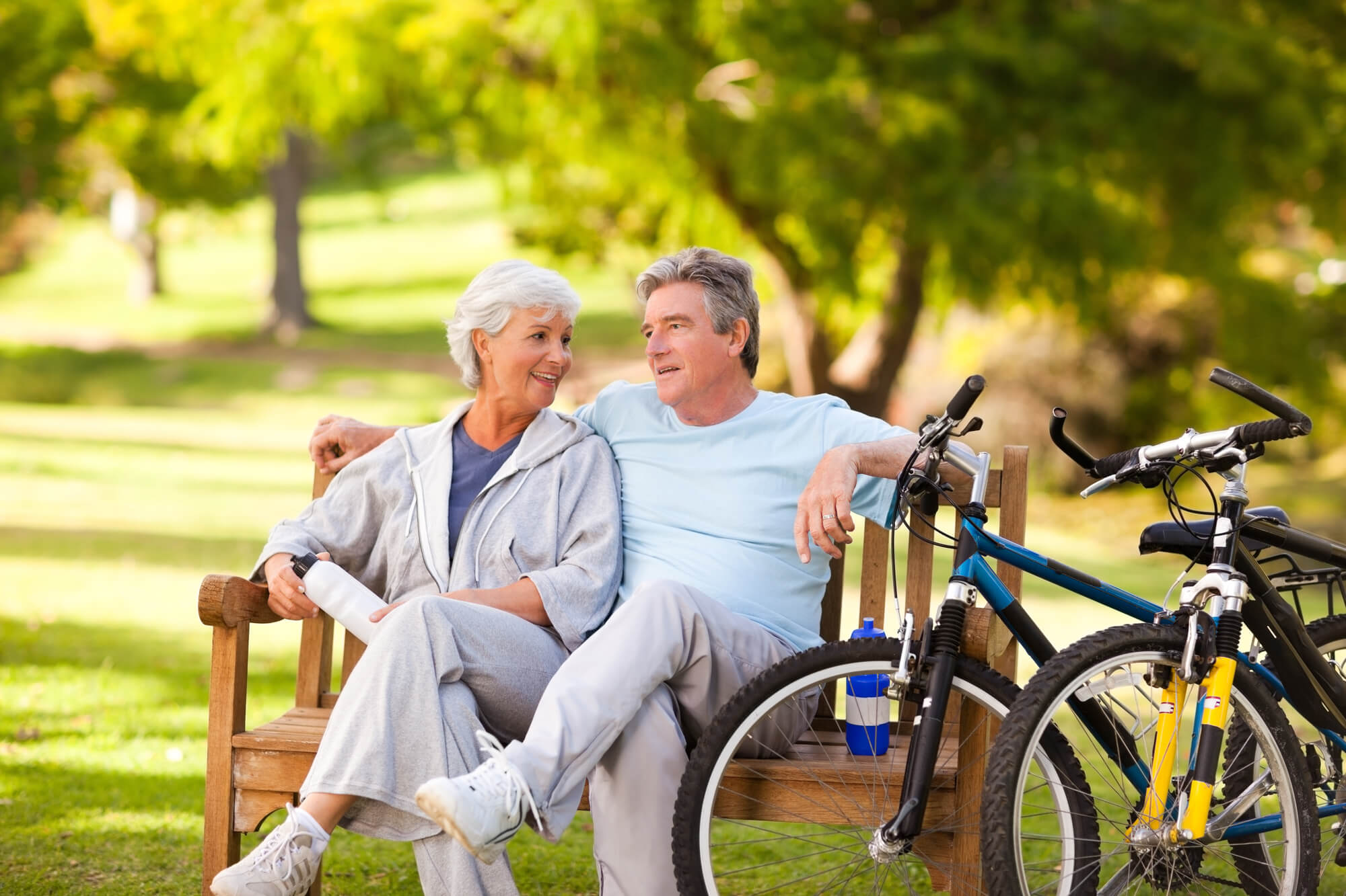 A couple taking a rest from biking on a bench. An older lady and an older gentleman