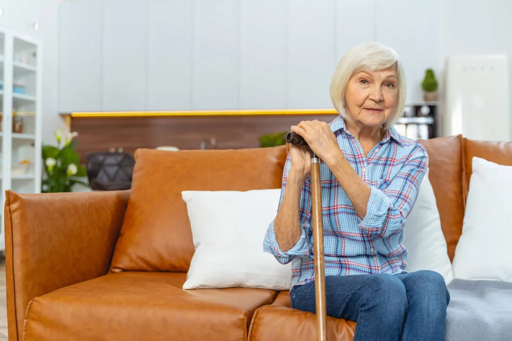 Old woman sitting on a couch, using her cane to sit up